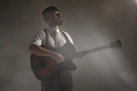 Fotografia de músico de jazz com guitarra acústica e visual retrô em estúdio esfumaçado.