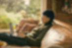 Person in a beanie, working on a laptop on a cozy couch. Greenery outside, warm light fills the room. Casual, relaxed atmosphere. The Magic of the Messy Middle: What It Really Takes to Scale