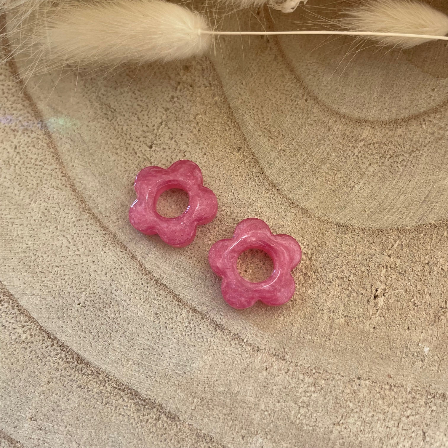 Deux charms en résine rose bonbon 🌸 en forme de marguerite, posés sur un support en bois naturel