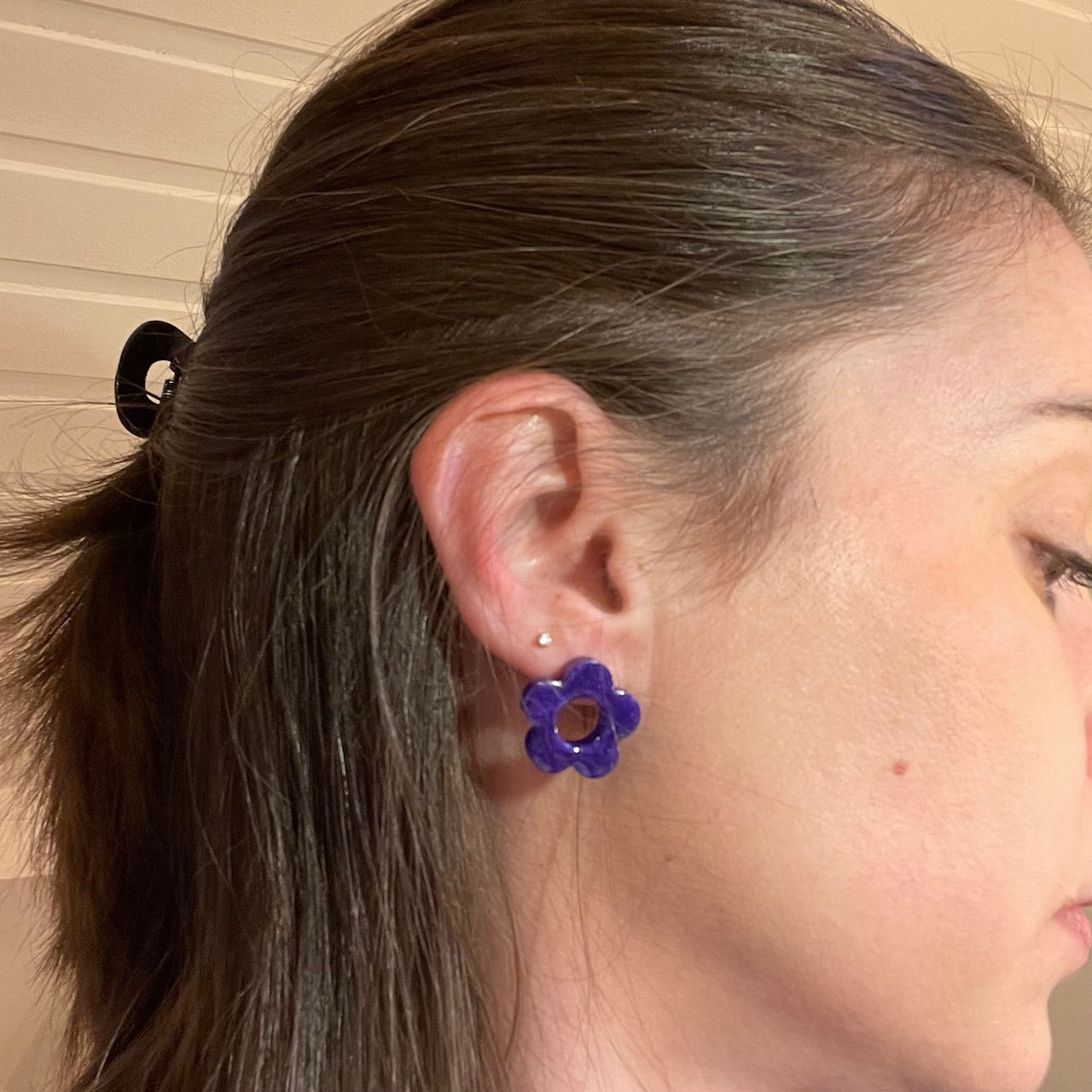 Gros plan sur une oreille portant une puce d’oreille en résine mauve en forme de marguerite.