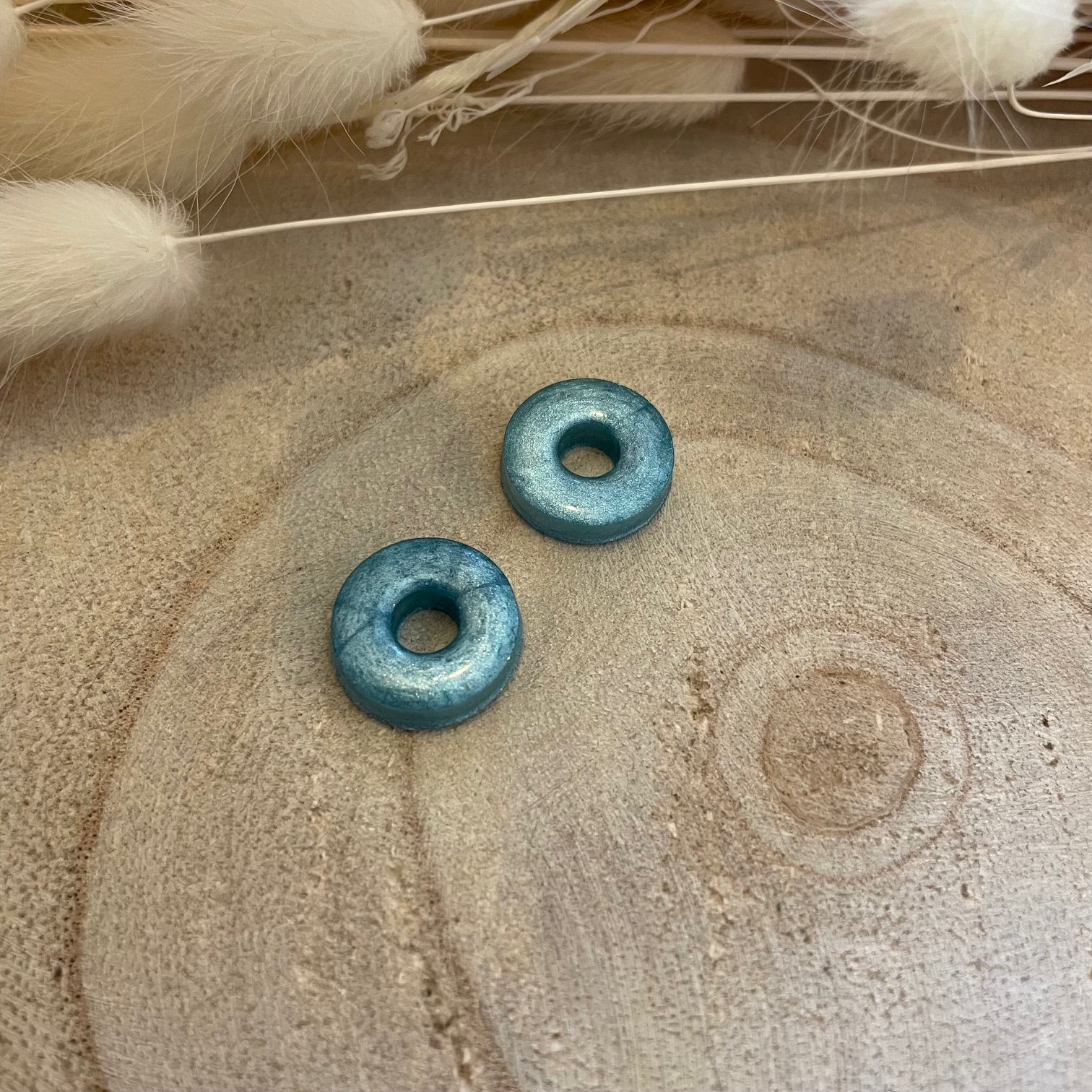 Paire de charms interchangeables en résine turquoise nacrée, posés sur un fond en bois