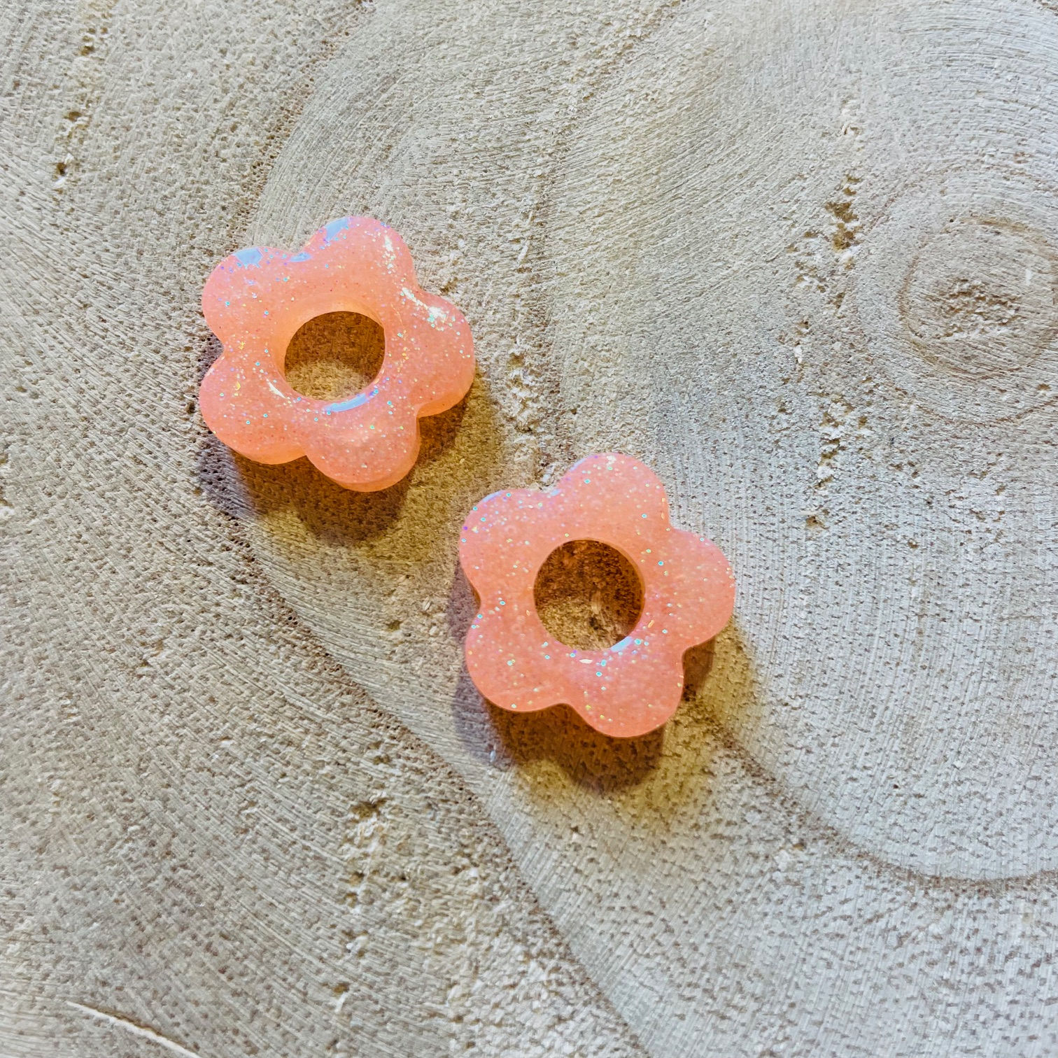Charms fleurs en pêche irisé scintillant, posés sur bois.