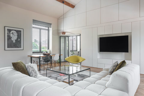 Espace de vie et de salle à manger lumineux avec des volumes blancs nets, un canapé sectionnel sculptural et un parquet à motif chevron. Des accents noirs graphiques, du bois chaud, un fauteuil jaune de déclaration et une lumière naturelle généreuse.