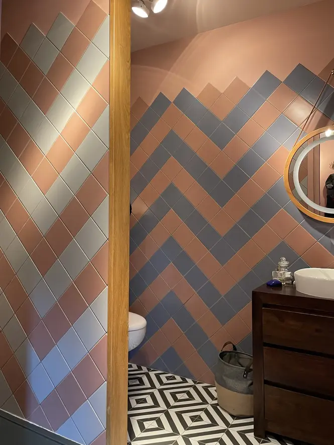 Salle de bains rénovée dans maison ancienne avec carrelage mural rose et bleu graphique, meuble vasque en bois foncé et sol géométrique.