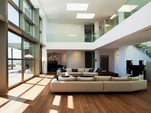 Salon contemporain lumineux avec double hauteur, grandes baies vitrées, canapé beige, escalier moderne en verre et bois, vue sur terrasse avec piscine.