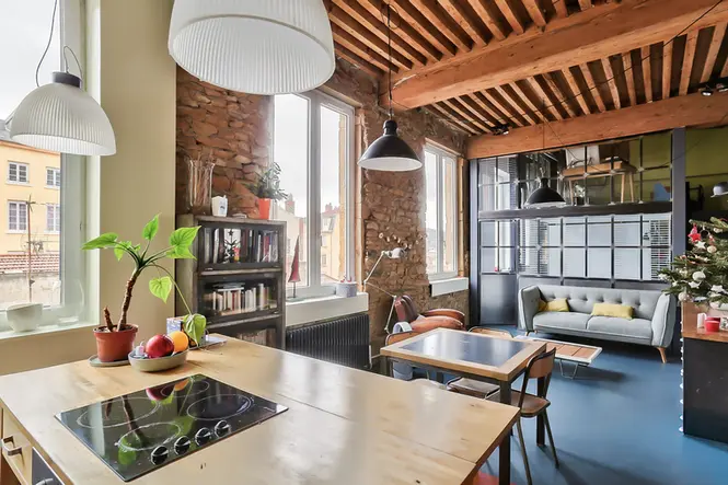 Cuisine ouverte avec verrière atelier, poutres apparentes et murs en pierre dans un loft rénové à Lyon Croix-Rousse