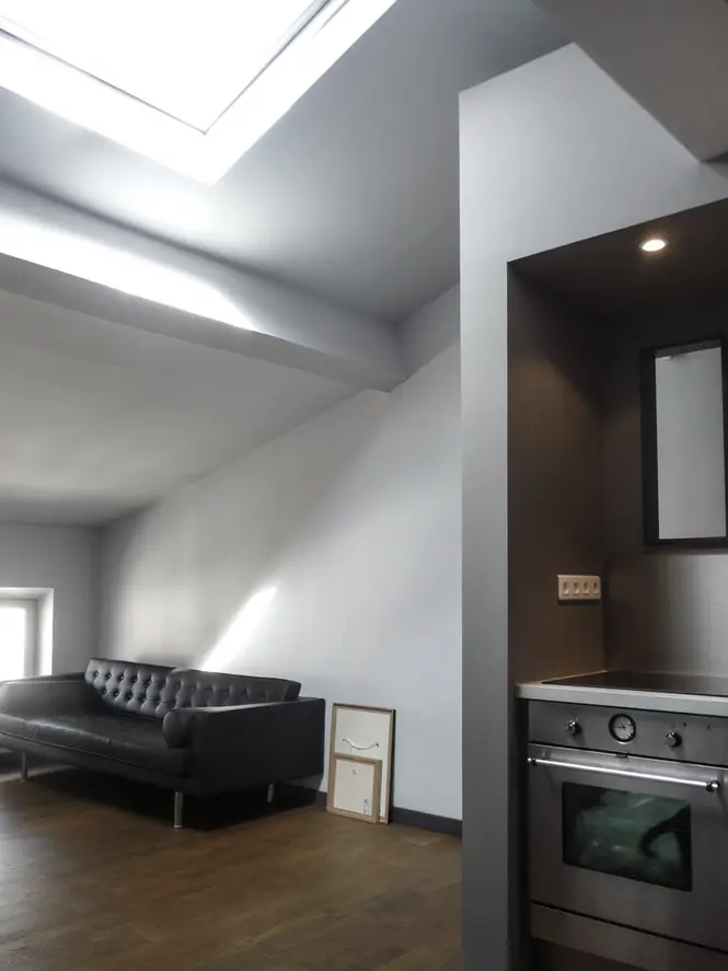 Cuisine ouverte contemporaine sous verrière zénithale avec mobilier minimaliste gris et optimisation des volumes dans un duplex rénové