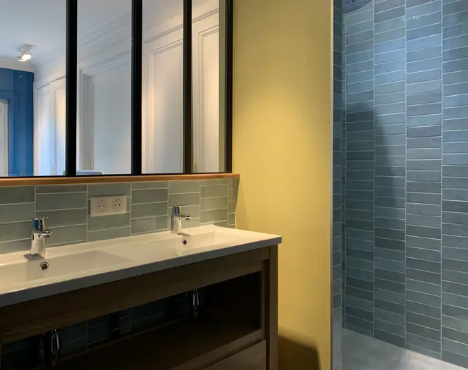 Salle d’eau contemporaine avec double vasque, carrelage bleu, douche italienne et verrière intérieure noire sur mesure.
