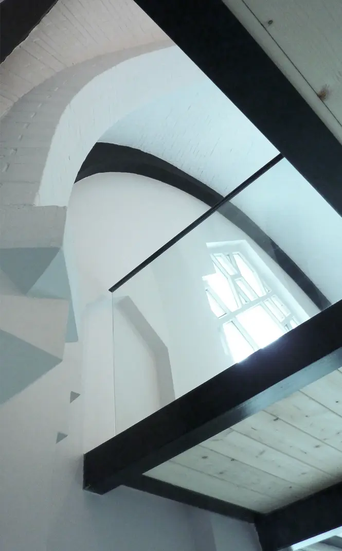 Mezzanine contemporaine avec garde-corps en verre et structure noire intégrée sous voûtes anciennes dans un appartement rénové.