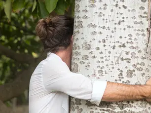Personne enlacant un arbre en extérieur, connexion à la nature, bien-être et environnement naturel apaisant.