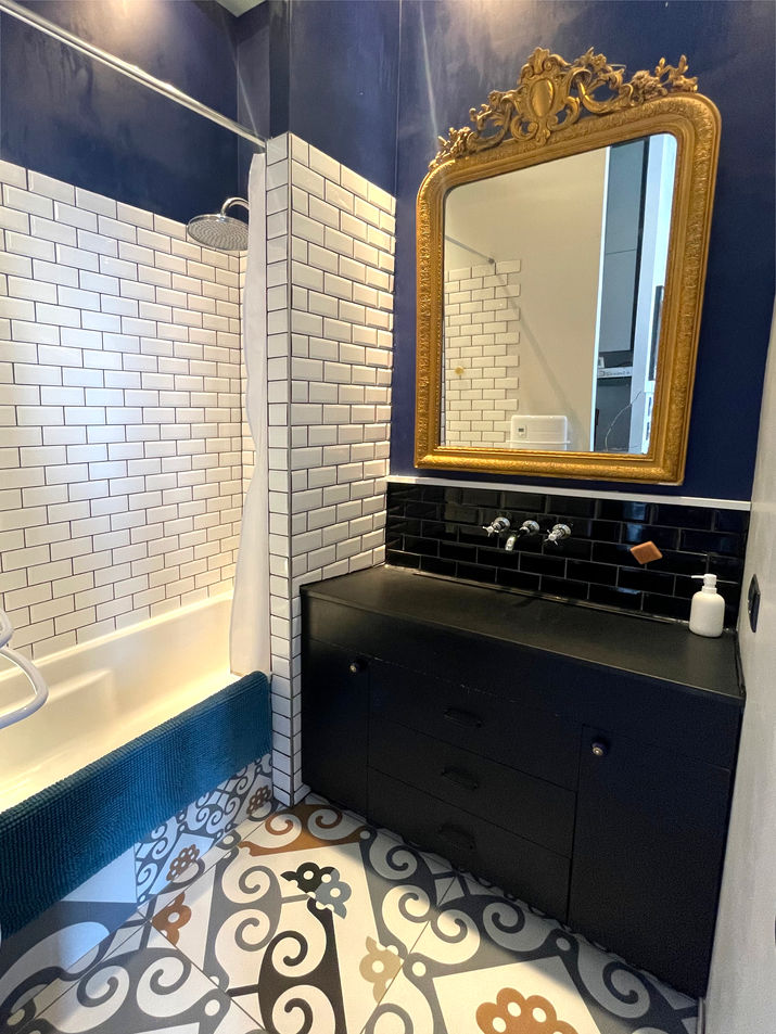 Salle de bain originale
	•	Sol : Même carreaux de ciment que la cuisine.
	•	Murs : Faïence blanche métro avec joint noir + peinture murale bleu nuit.
	•	Meuble vasque noir mat, robinet mural.
	•	Miroir : Très ornemental, doré à moulures baroques.
	•	Style : Mélange fort entre industriel, classique et contemporain.