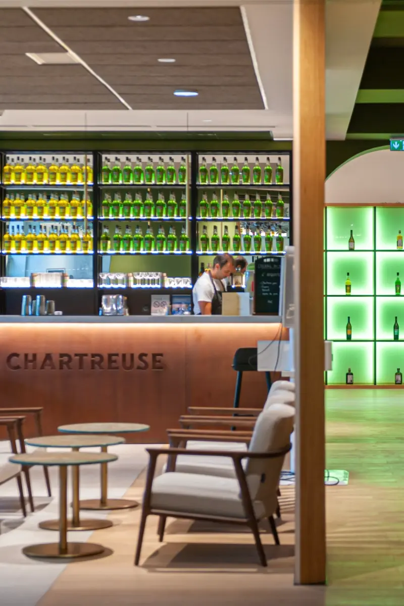 Espace daccueil et de vente avec bar retroeclaire mettant en scene les bouteilles de Chartreuse dans une ambiance elegante