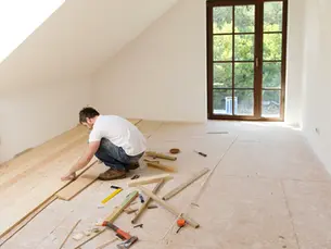 Pose de parquet dans une chambre sous combles, artisan travaillant le bois, rénovation intérieure avec lumière naturelle.
