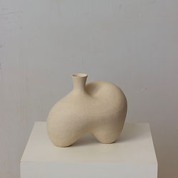 Two-legged off-white ceramic vessel with an asymmetrical curved form, displayed on a plinth against a white background.