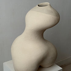 Large two-legged tall ceramic vessel made of white and grey stoneware, featuring an asymmetrical curved form, displayed on a white plinth against a white background.