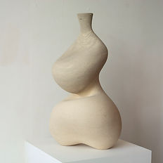 Two-legged tall off-white ceramic vessel featuring an inner groove and asymmetrical curved form, displayed on a plinth against a white background.