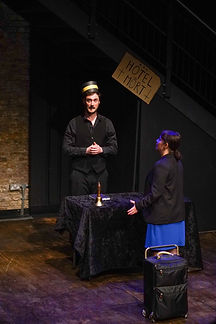 Paul Matania wearing a bell-hop hat, Anya Sayadian standing looking at him on stage