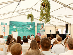 Photo intérieur de chapiteau durant un événement avec fond de scène, orateur au pupitre, participants assis en premier plan et décoration végétale dans le chapiteau