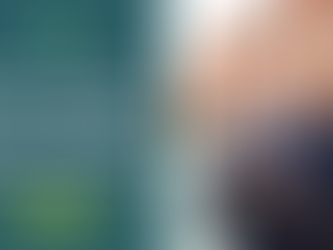 Smiling man in a suit holds keys outside, standing in a residential area with red brick houses. 