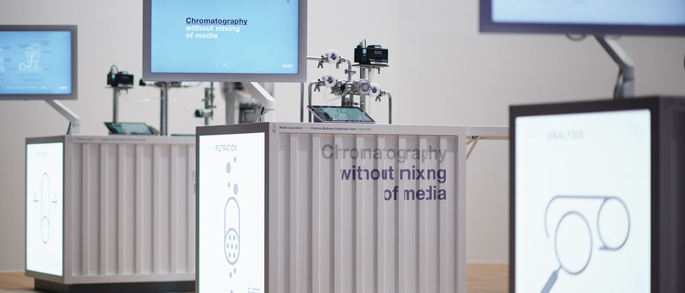 Bürkert Messestand : Detail der weißen Ausstellungstheken mit beleuchteten Fronten, technischen Geräten und Bildschirmen.
