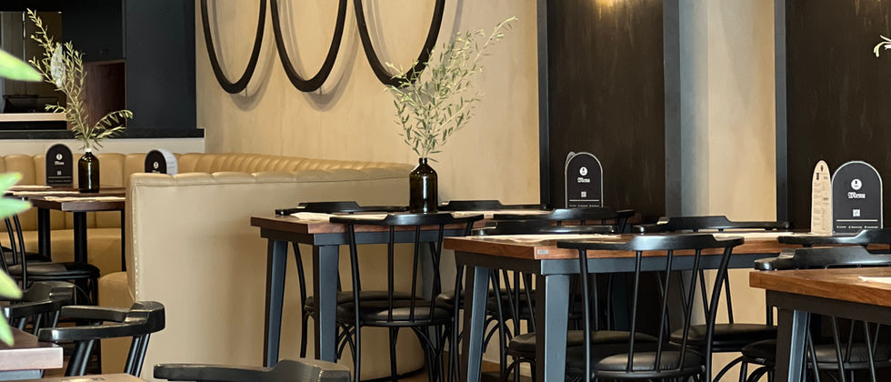 Mustache Restaurant : Seitlich aufgenommenes Foto der Tischreihen mit beleuchteten Menübogennischen und Deckendekoration aus Kochgeschirr.
