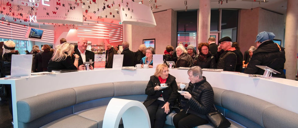Funke Medien Gruppe- Kiosk: Foto des belebten runden Sitzbereichs mit blau-grauen Polstern, Cafétheke und schwebenden Buchstaben.