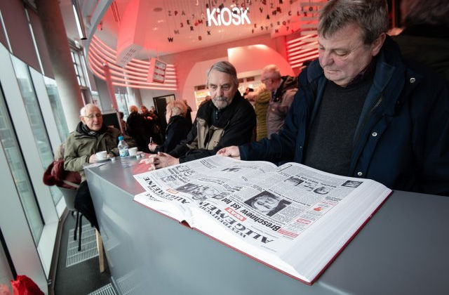 Funke Medien Gruppe- Kiosk: Foto von Besuchern beim Zeitungslesen an einer hellen Theke unter dem Kiosk-Schriftzug und hängenden Buchstaben.
