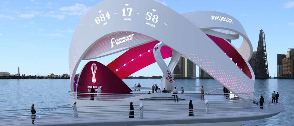 Countdown Clock World Cup 22: Tagesansicht der Installation mit Countdown-Ziffern, magentafarbener Schleife und Besuchern auf dem Vorplatz.
