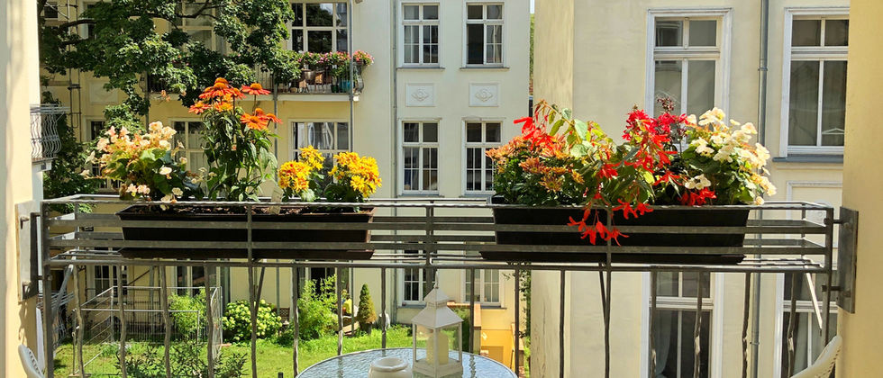 Wohnung Berlin Mitte: Foto eines Balkons mit rundem Glastisch, zwei Metallstühlen und bepflanzten Kästen vor der Hoffassade.