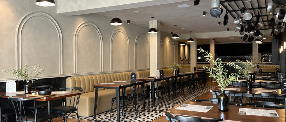Mustache Restaurant : Foto des Gastraums mit beiger Sitzbank, schwarzen Stühlen und an der Decke aufgehängtem Kochgeschirr.