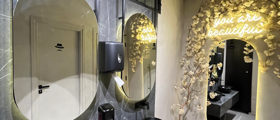 Mustache Restaurant : Zwei schwarze Aufsatzwaschbecken unter ovalen Spiegeln und einer goldfarbenen dekorativen Wandfläche.