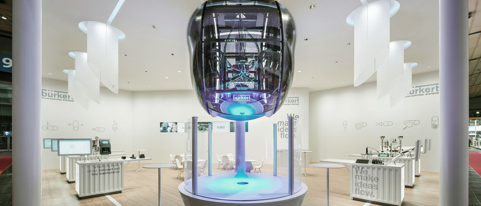 Bürkert Messestand : Nahansicht des zentralen technischen Exponats mit transparenter Hülle und blauem Licht.