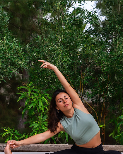 Daniela Hoyos Monroy en posture de yoga assise, un bras levé, dans un jardin