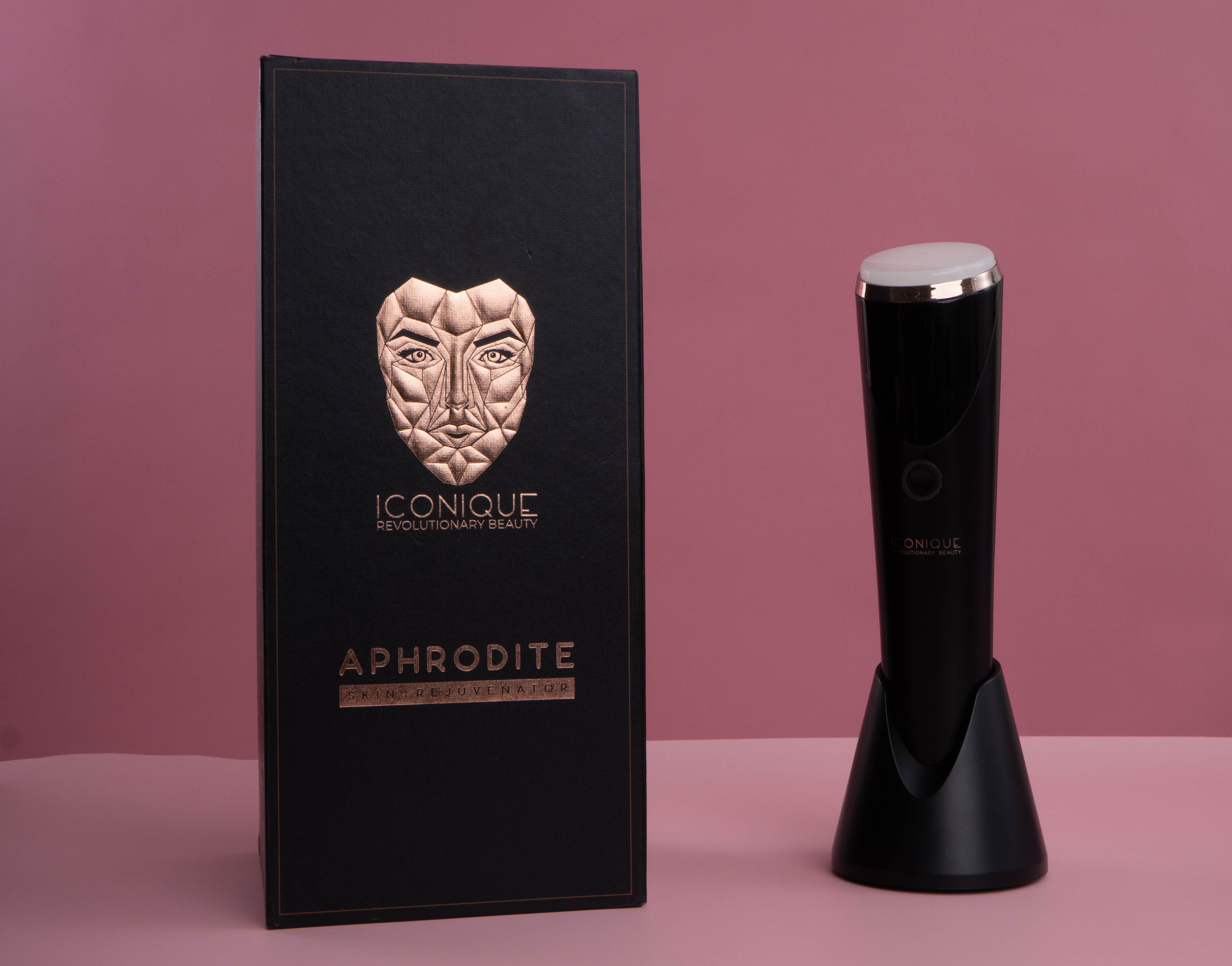 ICONIQUE Aphrodite skincare device displayed beside its black branded box on a soft pink background.
