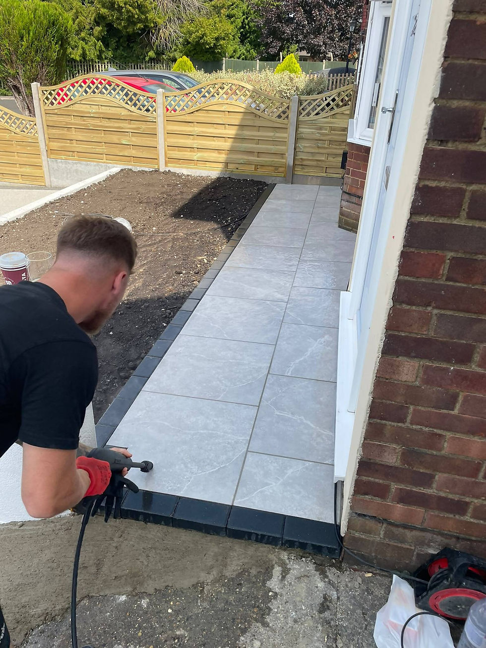 A man installs patio paving stones outside a brick house.