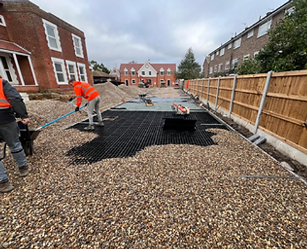 Two men are collaborating to install a gravel driveway, using tools and machinery for the task