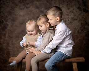 Familiefotografering i studie af 3 søskende. Billedet er i burnlige nuancer.