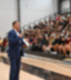 Principal Dr. Newsome addressing a full gray auditorium