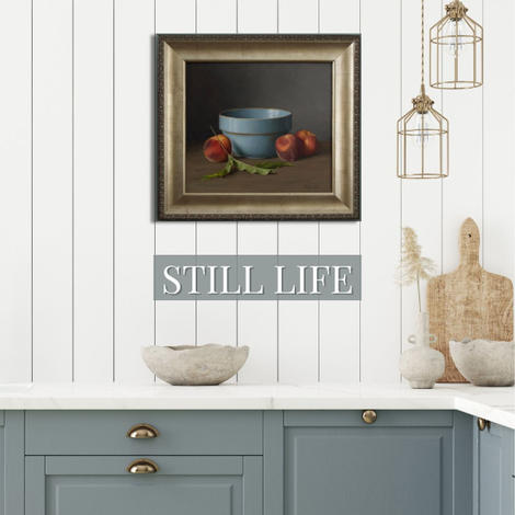 Kitchen with white bead board and blue cabinets with a still life painting of a blue bowl holding peaches by artist Cecelia Cox
