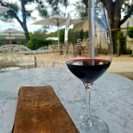 Wine glass from signor winery with red wine in it sitting on an outside table.