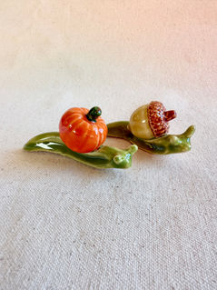 two handmade ceramic snails with whimsical shells that look like a pumpkin and an acorn
