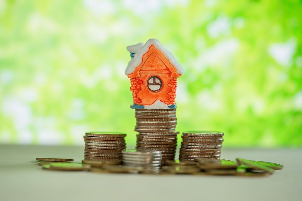 A small orange house model sits on stacks of coins against a blurred green background, symbolizing savings or investment.