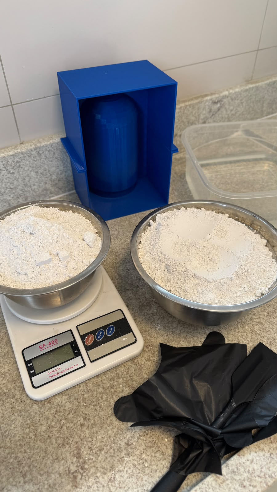 Gesso sendo pesado em balança digital ao lado da matriz 3D montada na caixa de contenção azul.