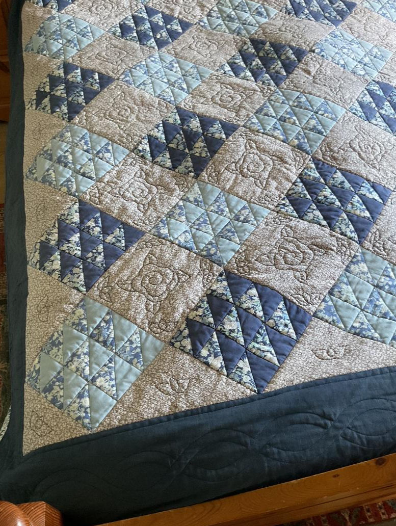 Detail of border, the hand quilting of roses and buds on patchwork quilt.