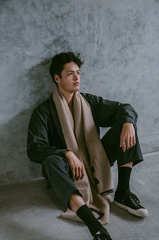 Corban Tupou sitting with concrete background wearing a Dark Hampton Scarf