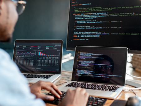 Programador digitando em três telas com código e gráficos de dados, em escritório moderno, clima focado.