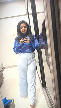 Woman taking a mirror selfie in a blue patterned top and white wide-leg trousers