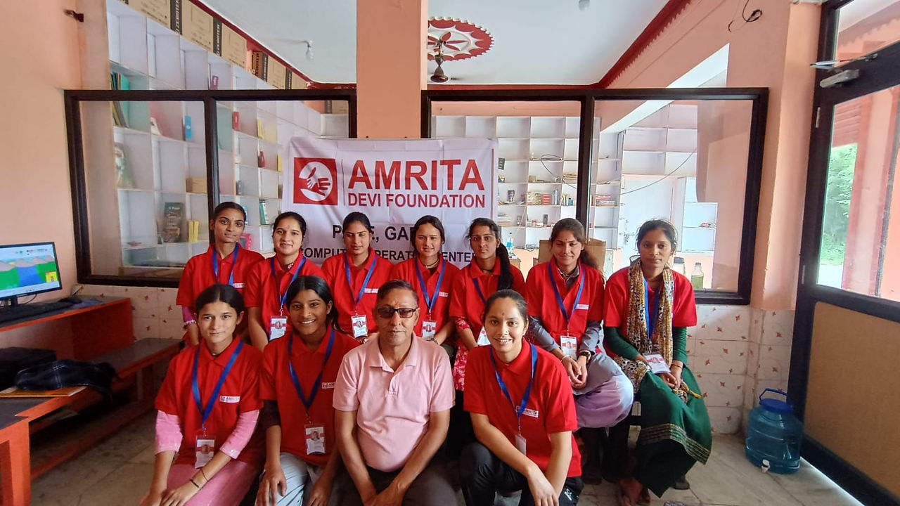 Group photo, Amrita Foundation banner. Women and girls in red shirts smiling.