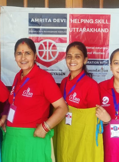 Five women in colorful skirts and red shirts pose in front of a building.