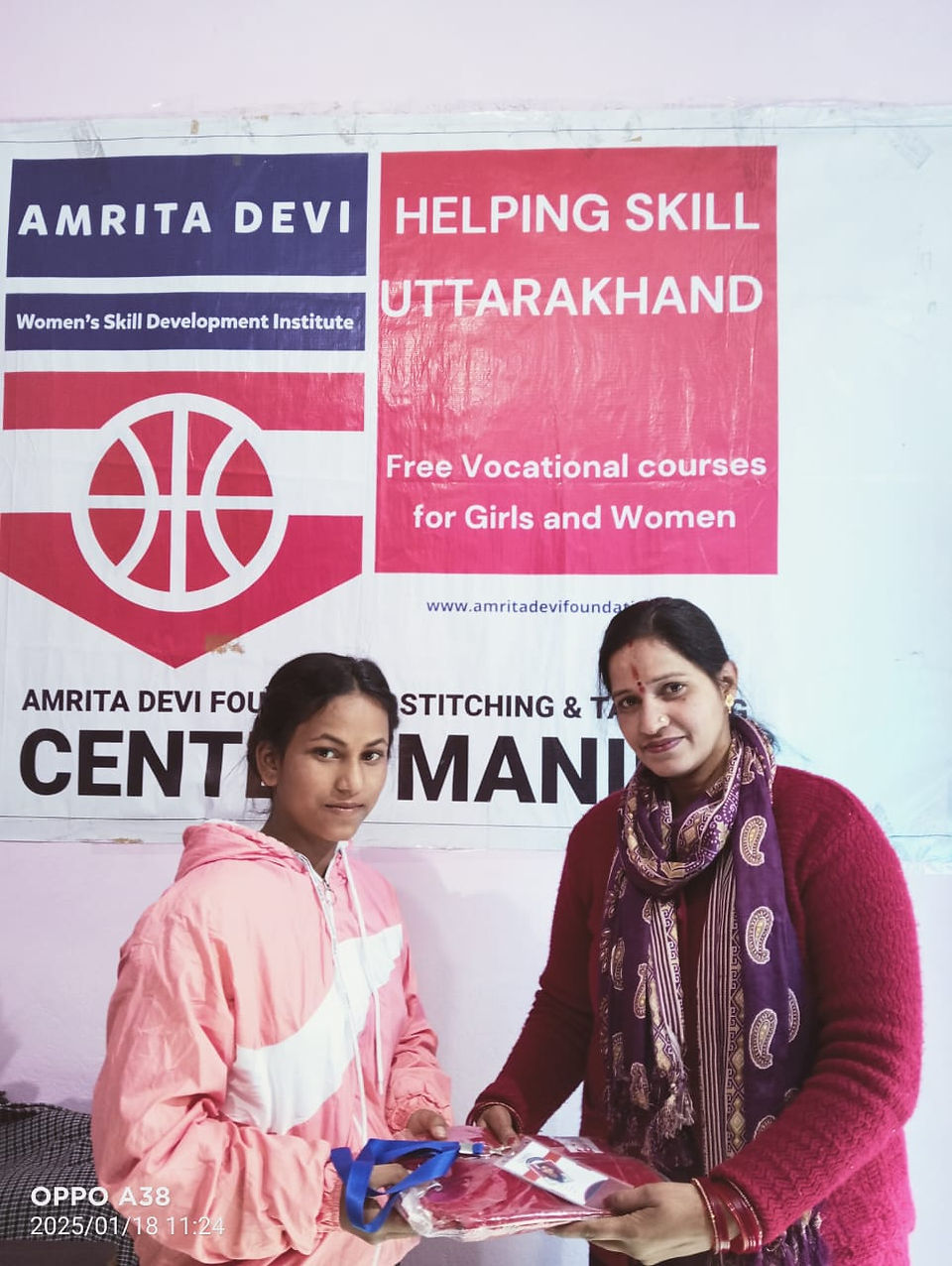 Two women in front of a banner; Amrita Devi and Helping Skill Uttarakhand.